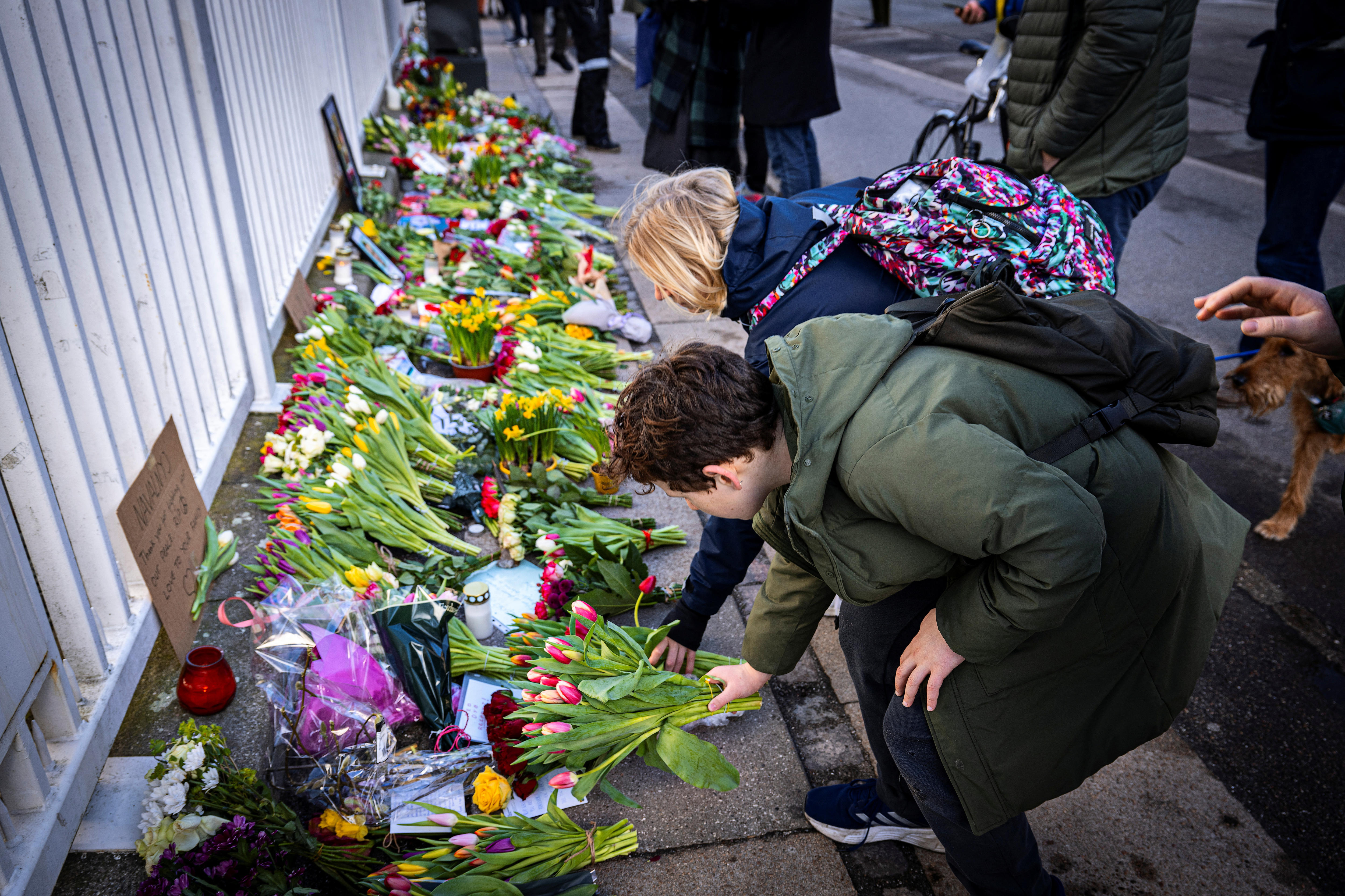 People bend down to lay flowers at the foot of a fence.