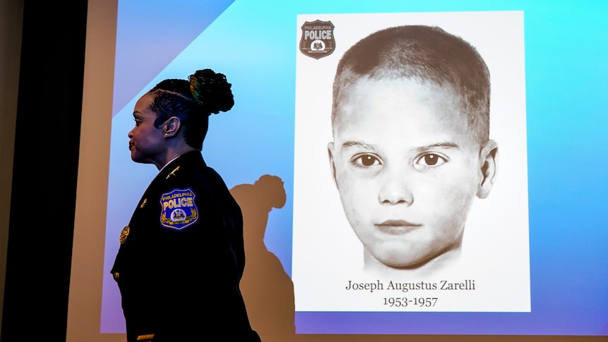 A woman in a police uniform walks past a projected image of a black and white photo of a boy