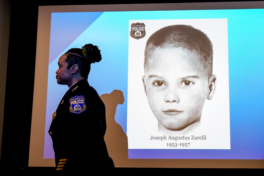A woman in a police uniform walks past a projected image of a black and white photo of a boy