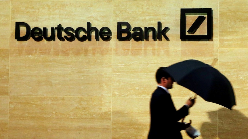 A man walks past a Deutsche Bank logo on a wall.