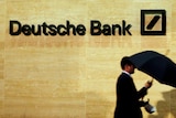 A man walks past a Deutsche Bank logo on a wall.