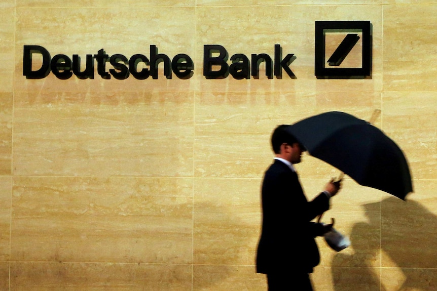 A man walks past a Deutsche Bank logo on a wall.