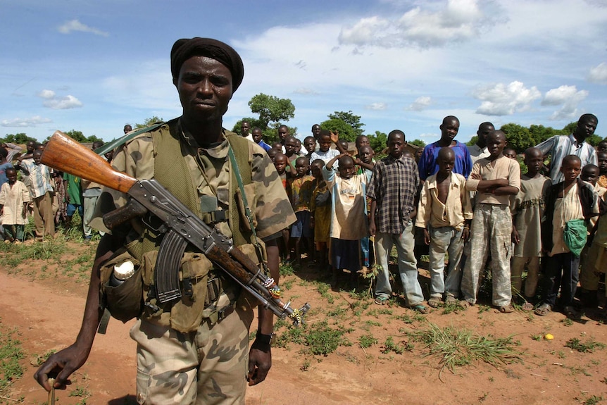 Armed militia man standing in front of a group of African adults and children