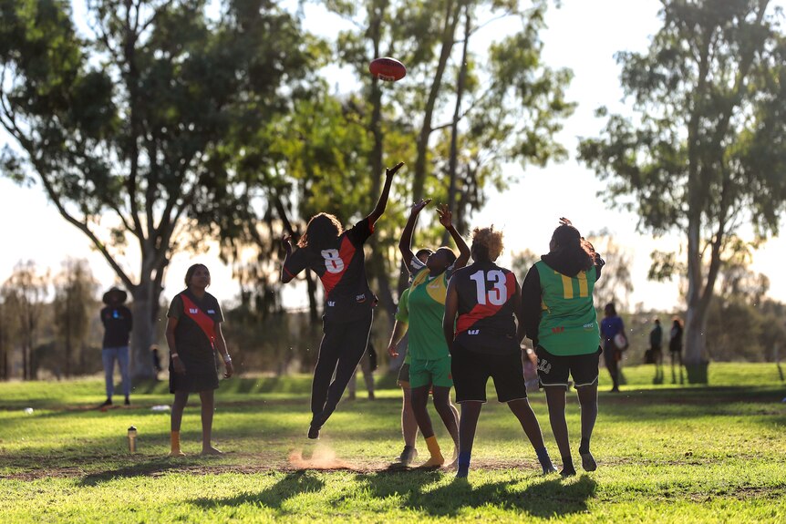 Young Aboriginal women jump for a football on a green oval in the late afternoon sun