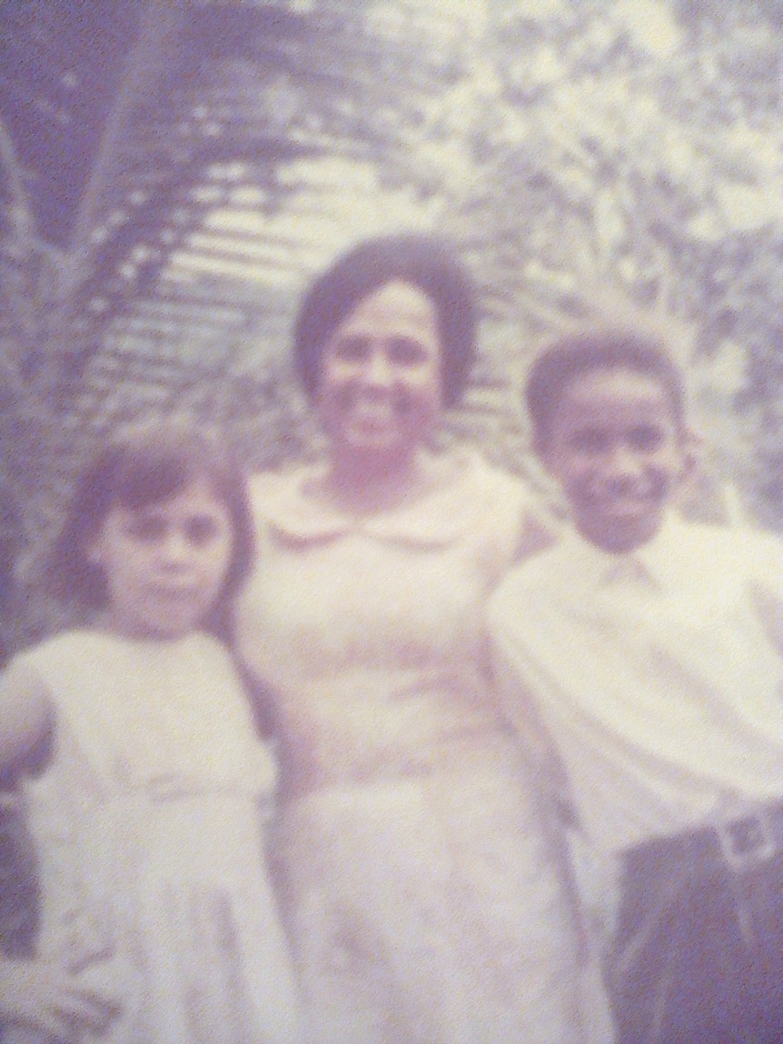 A grainy photograph from the late 1970s shows three children smiling at the camera.