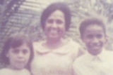 A grainy photograph from the late 1970s shows three children smiling at the camera.