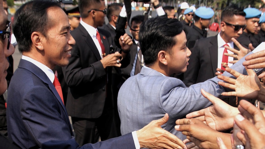 Joko Widido left shakes hands with a crowd of supporters next to his son who is also greeting people.