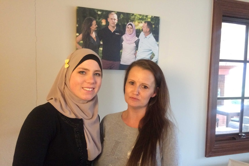 Two women standing next to each other in front of a family photo