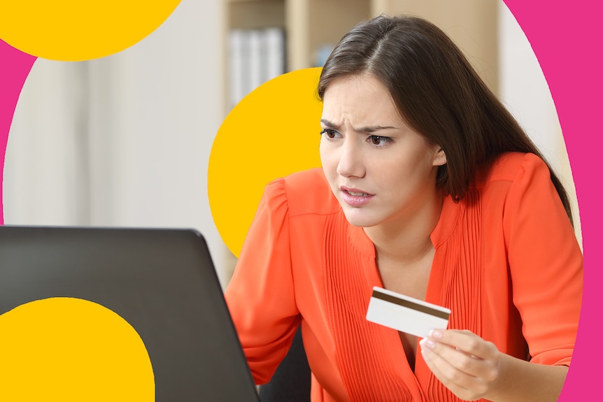A stressed woman looks at a laptop, holding up her credit card.