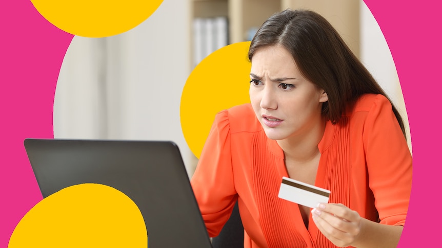 A stressed woman looks at a laptop, holding up her credit card.