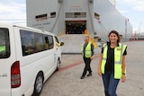 A smiling woman and man walk to a car in high-viz vest on at a dockside