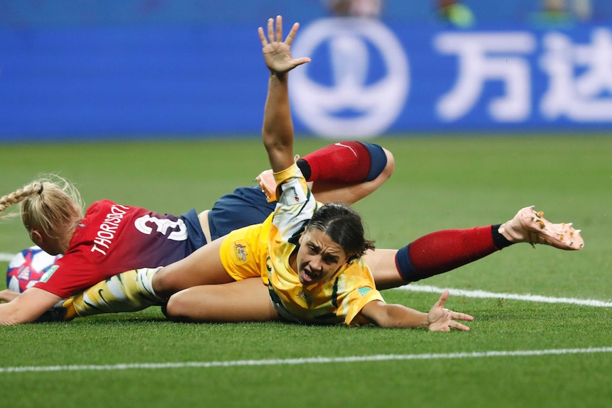 Australia's Sam Kerr is on her stomach on the ground, with Thorisdottir still on top of her, her arms raised in protest