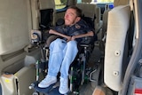 A young man in jeans sits smiling in a motorised wheelchair in the back of a accessible van.