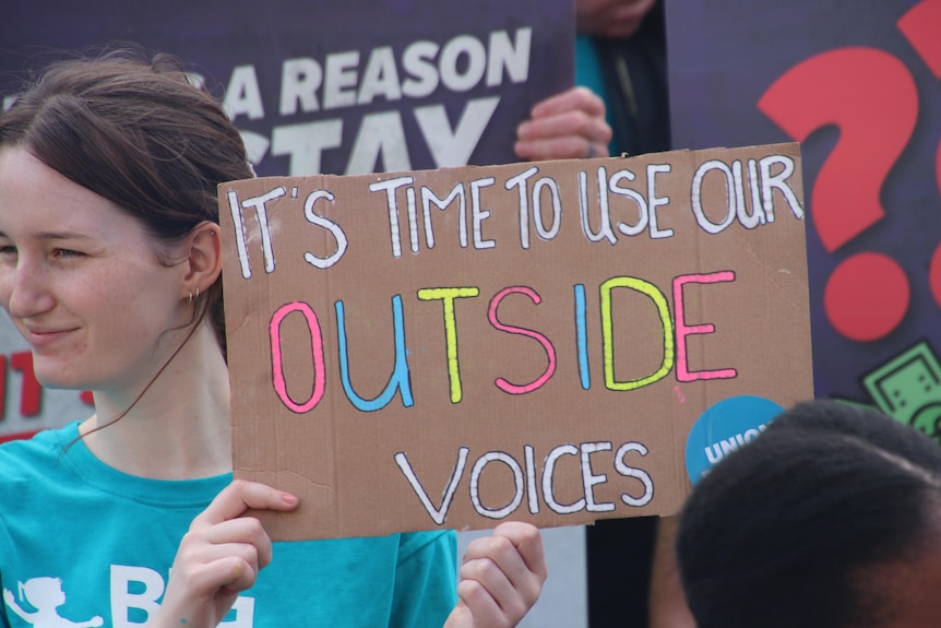 a woman holds a sign that says "it's time to use our outside voices"