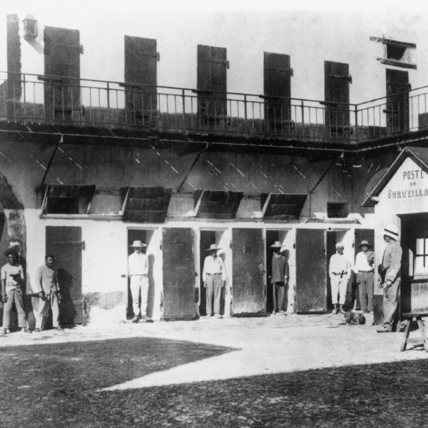black and white image of men lined up in a row of doorways in the courtyard of a stone walled building