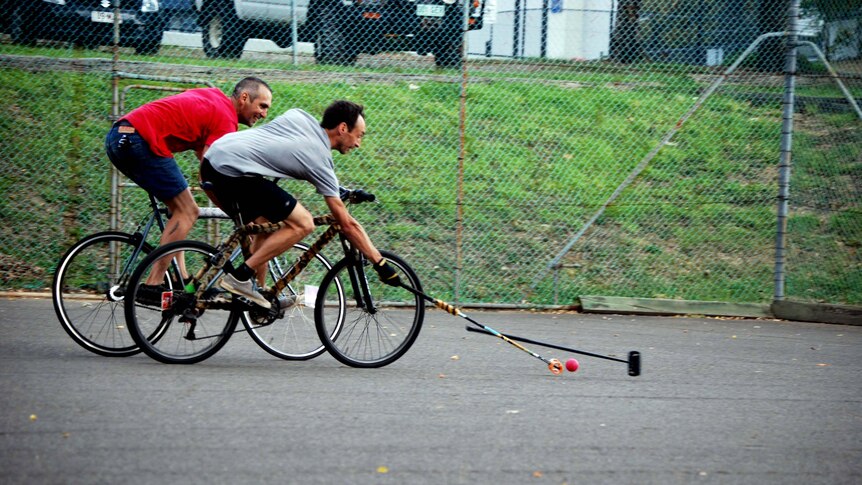 Bike polo players reach for the ball with their mallets