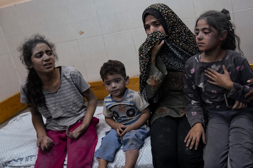 A woman and three girls sit on a hospital bed covered in dust.