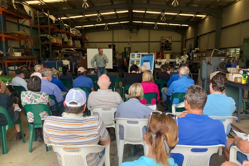 A group of people gathered in a shed for a talk.