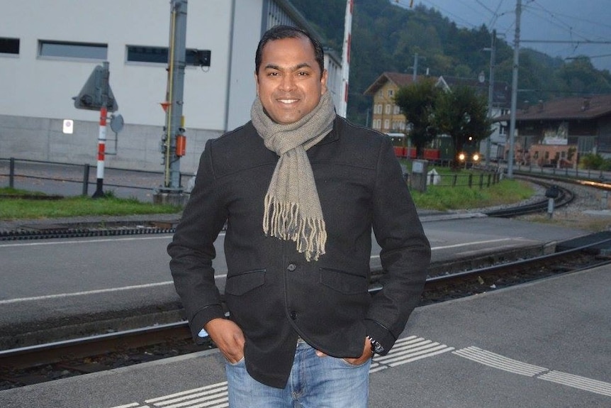 A man wearing a jacket, scarf and jeans near a railway line