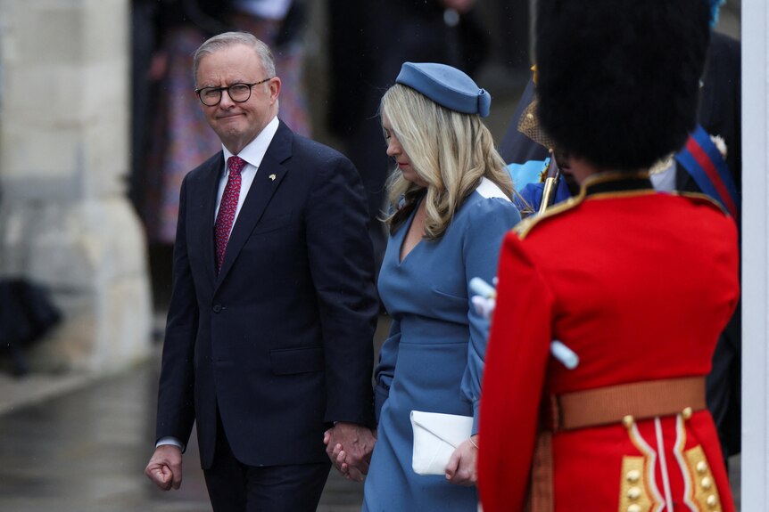 Anthony Albanese in a navy suit next to a blonde woman in blue behind a guard.