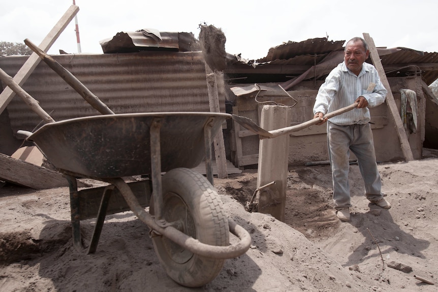 A man shovels dirt into a wheelbarrow.
