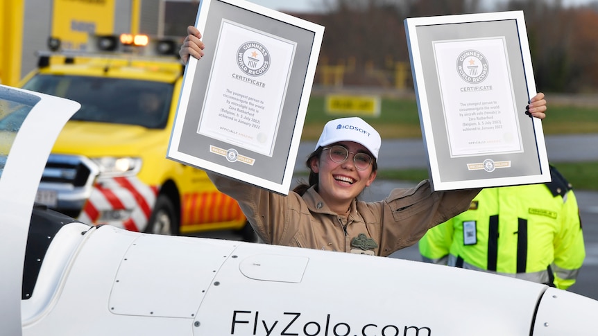 Girl stands in plane holding up certificates