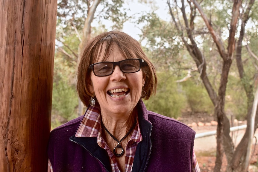 A lady with brown hair and wearing glasses smiles at the camera