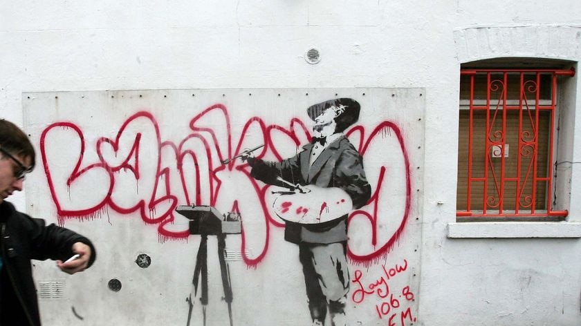 A man walks past a graffiti mural by British artist Banksy