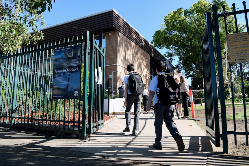 students carrying back packs walking through the school gates