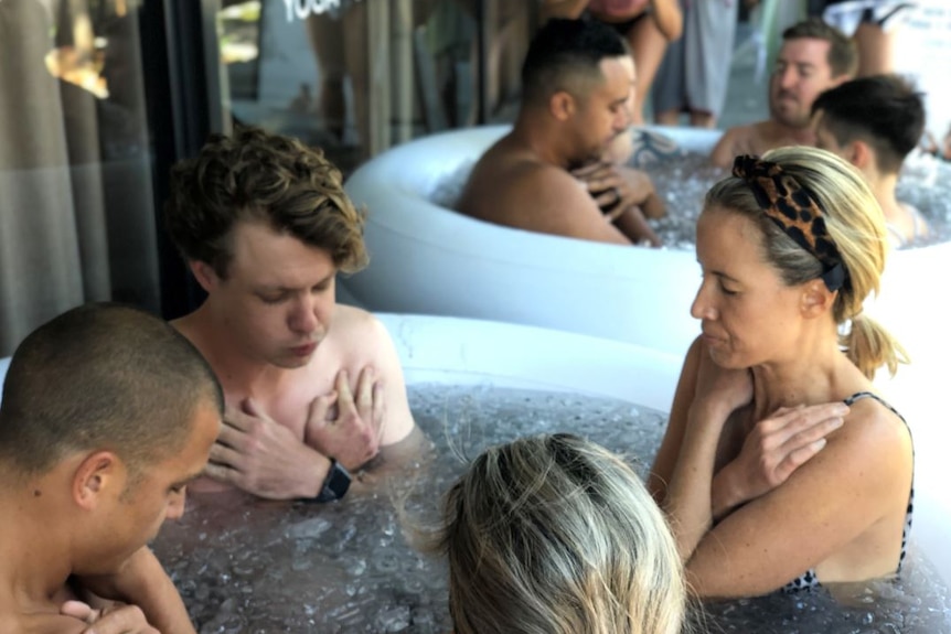 People sit in an inflatable bath filled with ice to their chests and close their eyes with their arms folded across their chest