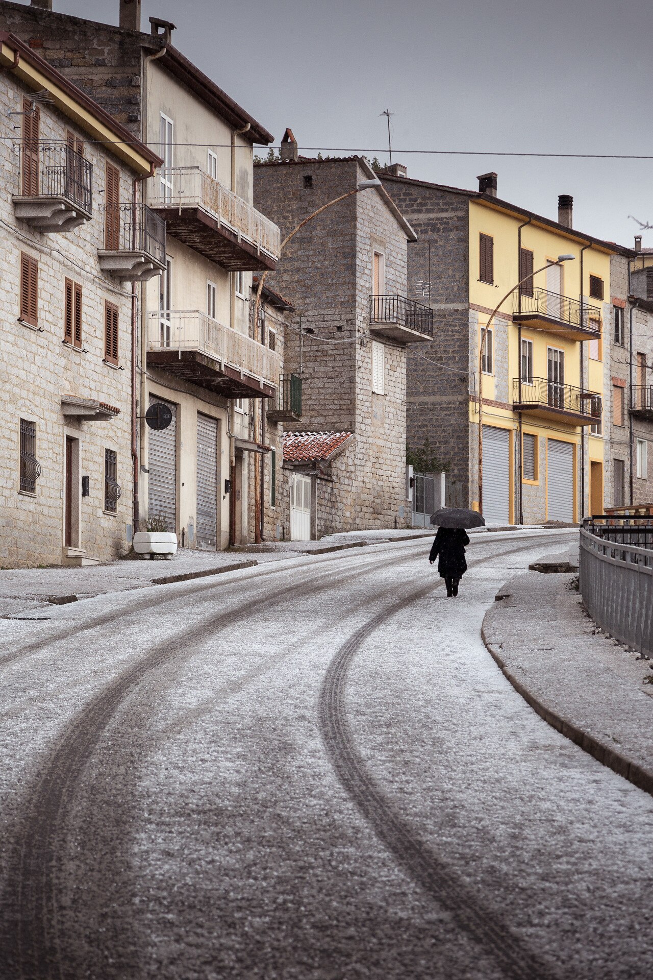 A person walks down an empty street lined with snow and bright buildings on either side.