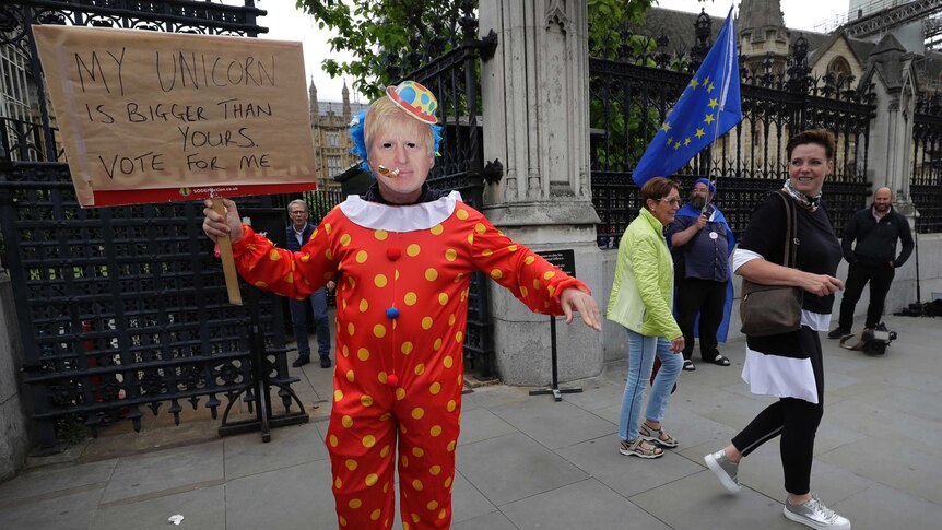 A demonstrator in a Boris Johnson mask and a clown suit stands outside UK Houses of Parliament.