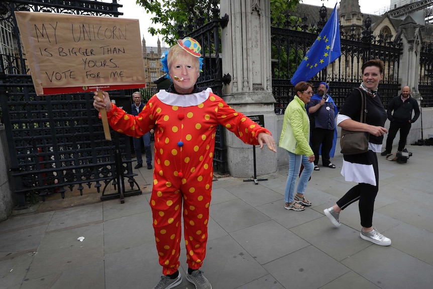 A demonstrator in a Boris Johnson mask and a clown suit stands outside UK Houses of Parliament.