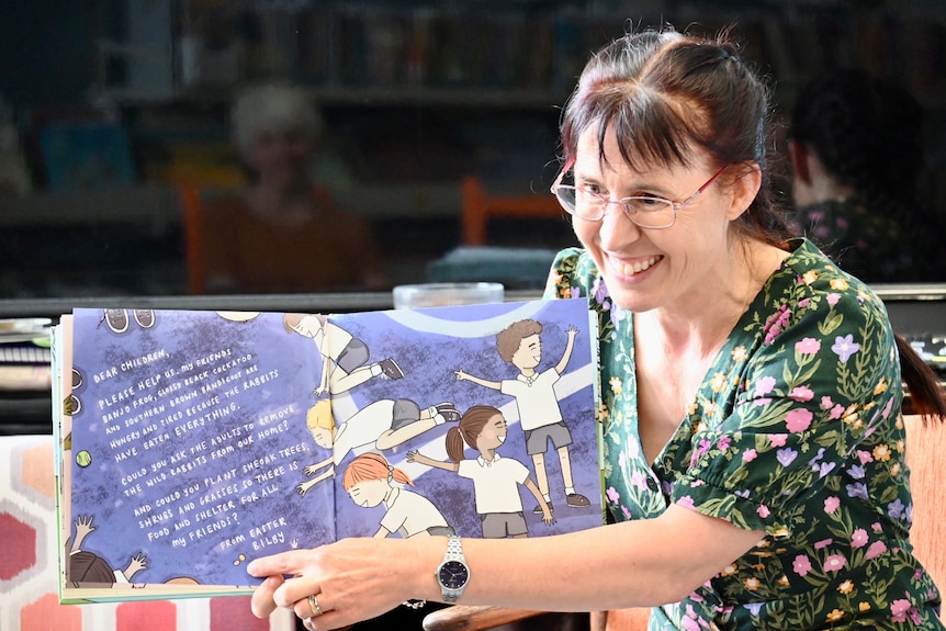 A woman holds a picture book open and points to the words on a page