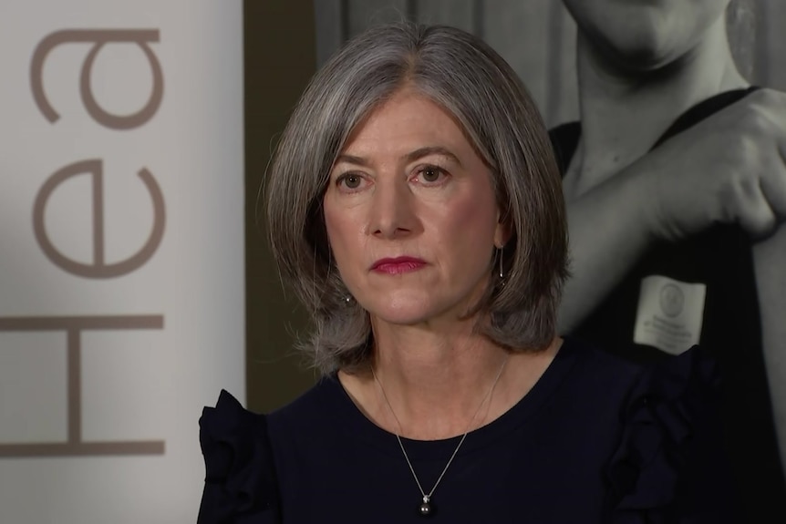 A close up of a woman with grey shoulder-length hair with a serious expression