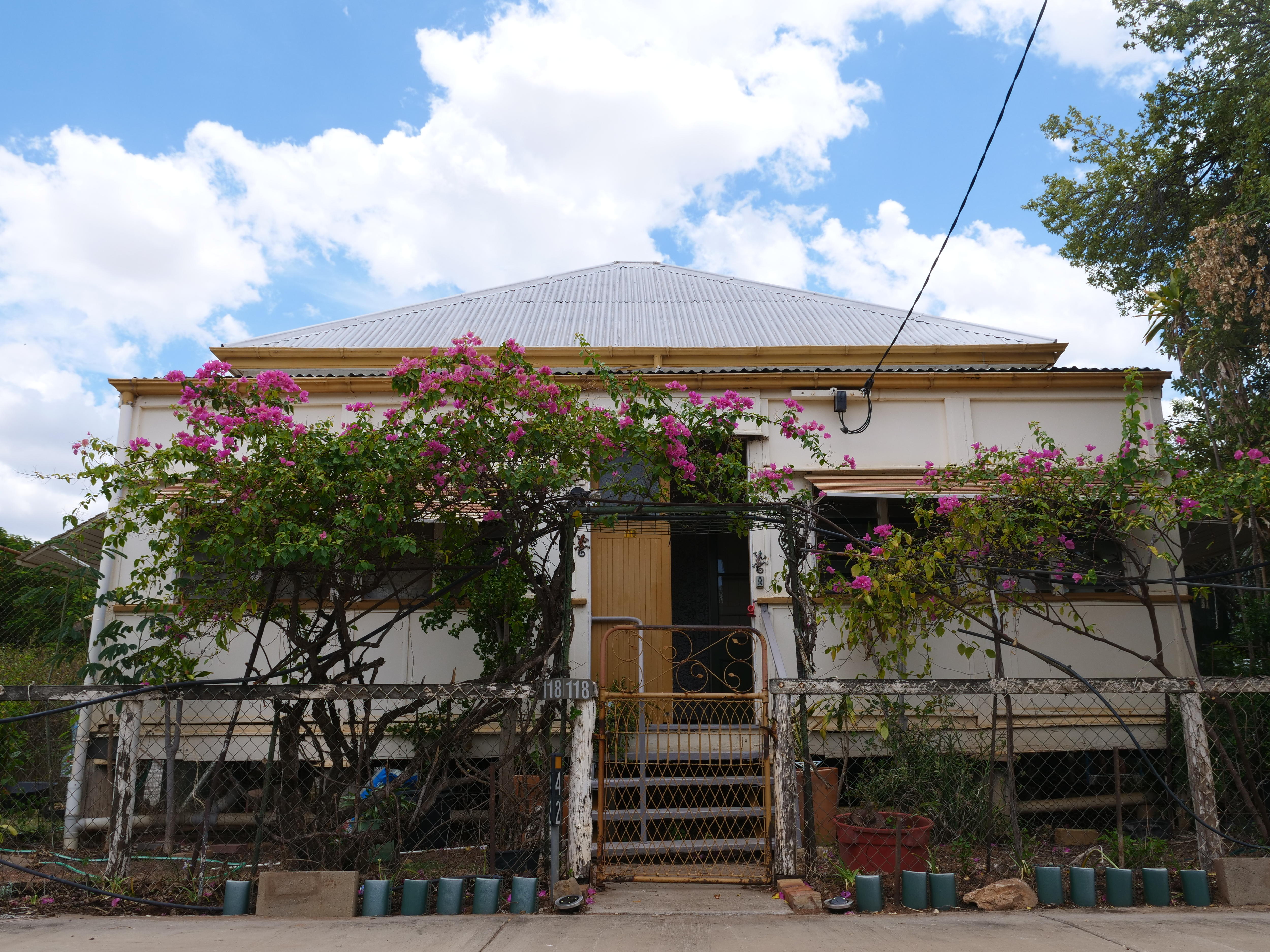 Cabaña blanca y amarilla de los años 40 con enredaderas verdes y rosas en la valla delantera