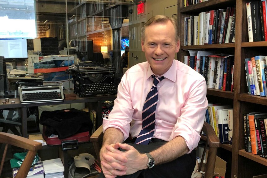 American journalist John Dickerson, a co-host of CBS This Morning. He is sitting in an office beside a bookshelf.