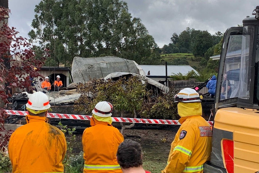 Firemen and workers stand around a house gutted by fire at Geeveston in Tasmania.