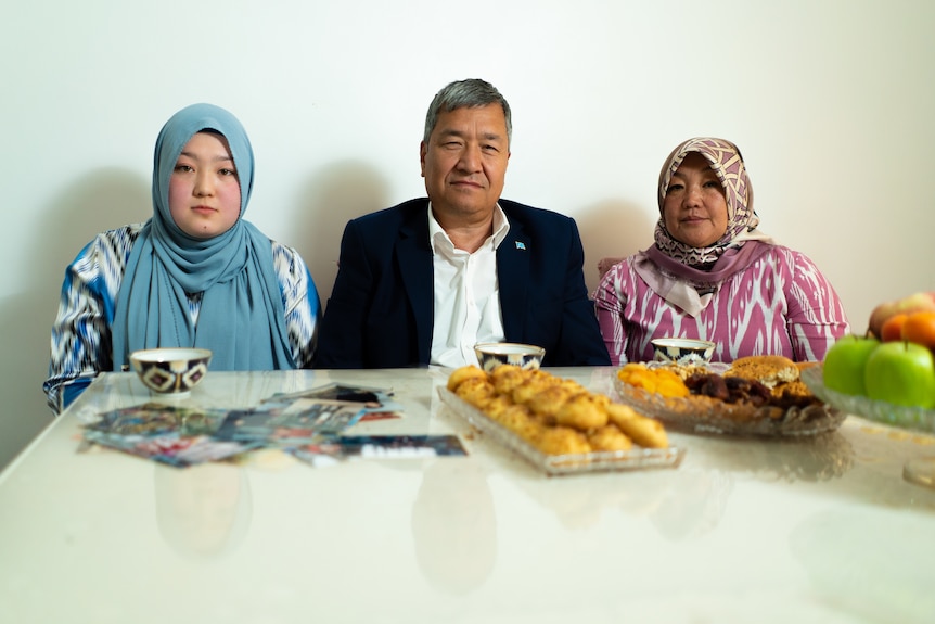 A young woman sits at the family table besides her father and mother.