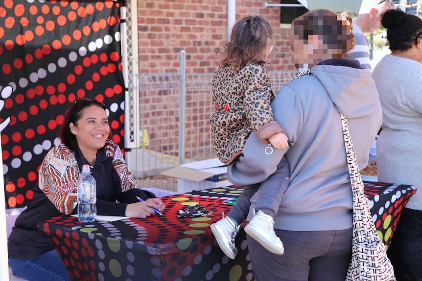 A woman sitting at a table, talking to another woman who is holding a small child.