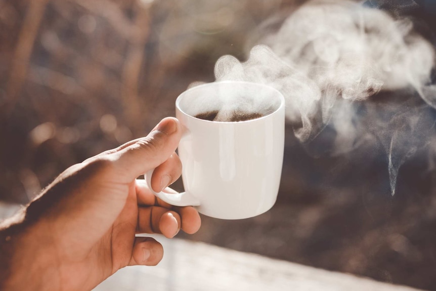 A hand holding a white mug with a dark and steaming liquid in it.