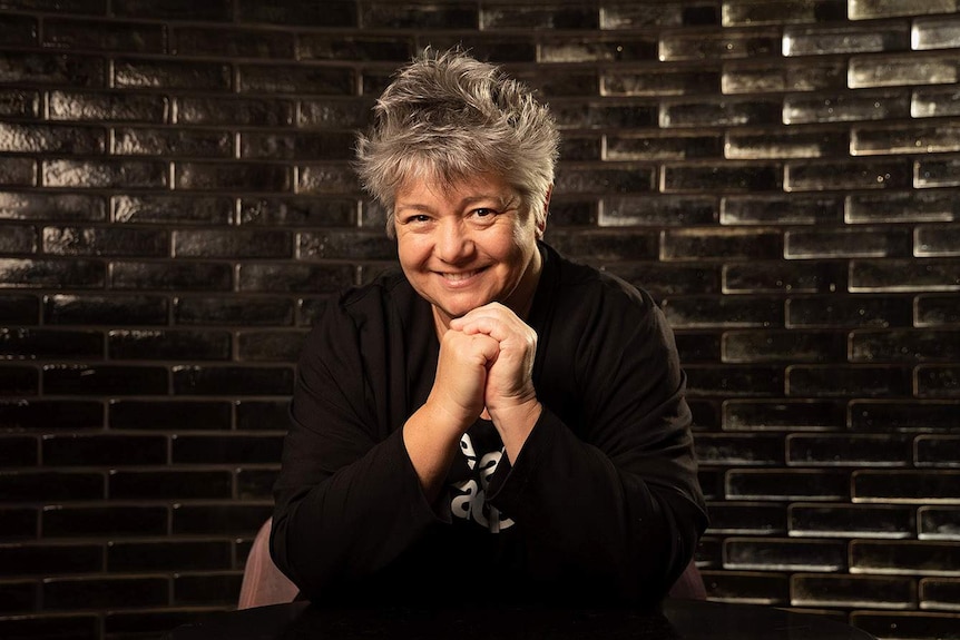 The author sits, with her chin in her hands, smiling at the camera in front of a wall covered in black tiles.