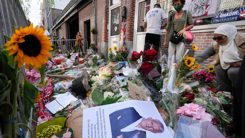 People add to piles of flowers and  tributes in an Amsterdam street.