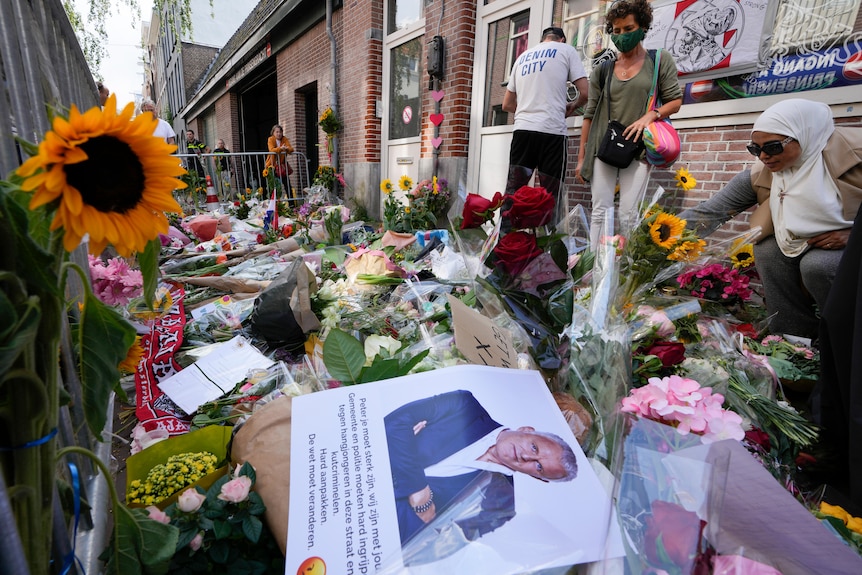 People add to piles of flowers and  tributes in an Amsterdam street.