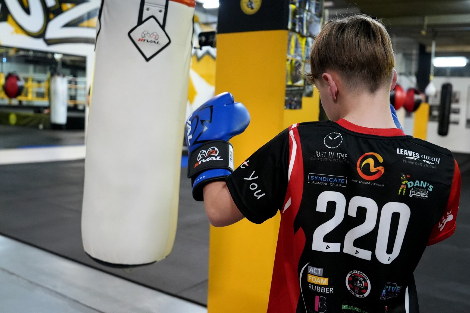 A child in a sports jersey punches a punching bag. 