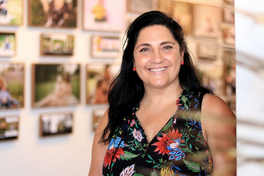 A smiling woman stands in a gallery with photos behind her