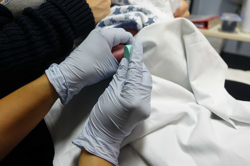 A midwife pricks a newborn's foot.