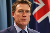 A tight head and shoulders shot of Attorney-General Christian Porter with an Australian flag over his left shoulder.