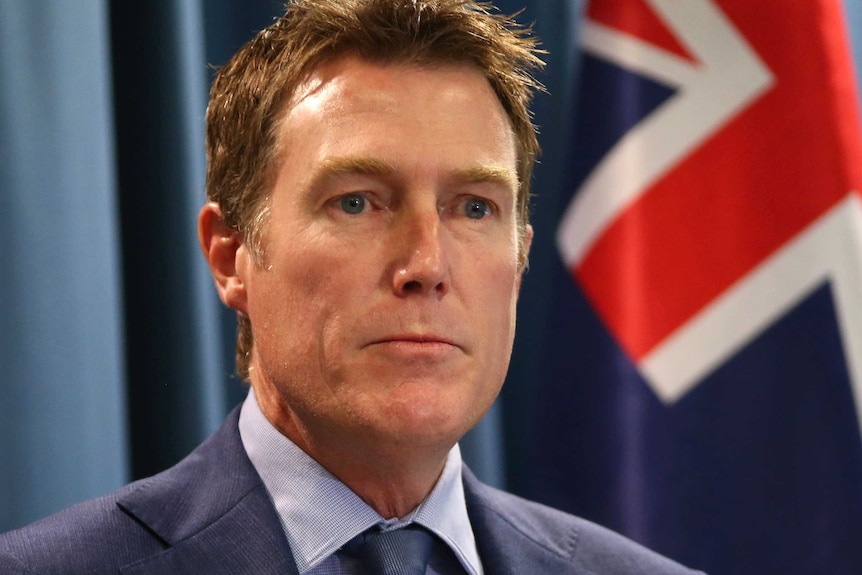 A tight head and shoulders shot of Attorney-General Christian Porter with an Australian flag over his left shoulder.