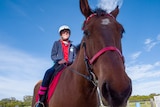 Close up of brown horse, with rider Aleisha on the saddle, she is smiling and wears a red shirt and blue jacket.